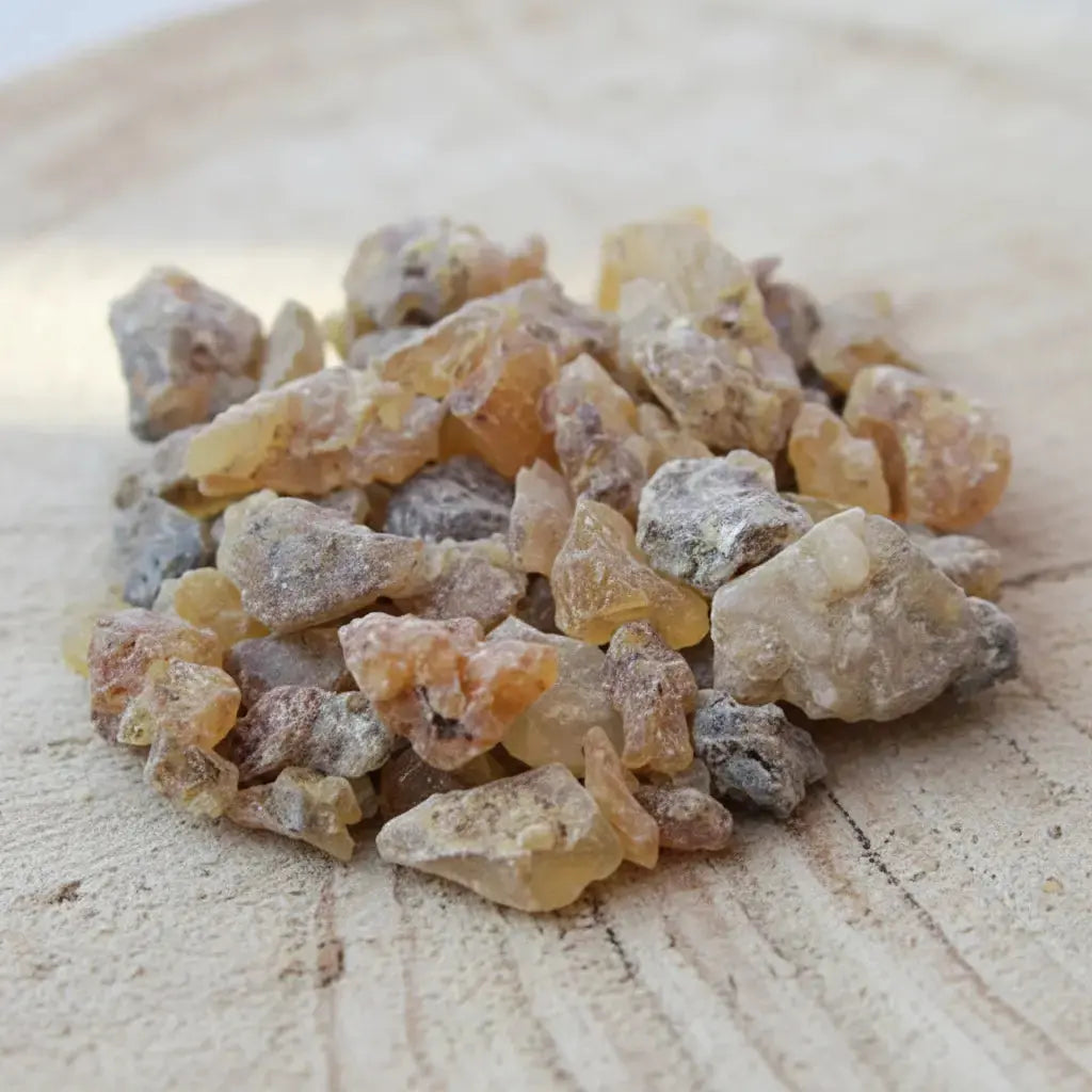 Gros plan sur des grains de résine d’encens copal clairs et irréguliers sur fond en bois clair.