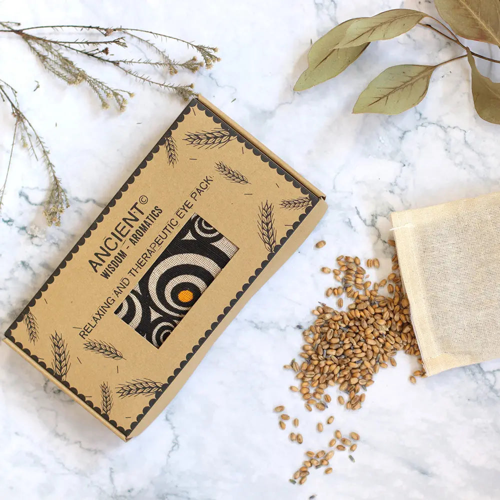 Masque de détente yeux motif cercles dans sa boîte avec grains naturels sur fond marbre et feuilles séchées.