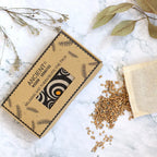 Masque de détente yeux motif cercles dans sa boîte avec grains naturels sur fond marbre et feuilles séchées.
