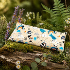 Coussin chauffant rectangulaire aux motifs de pandas, arcs-en-ciel et étoiles, posé sur un tronc d'arbre moussue en pleine nature, entouré de fleurs sauvages et de fougères.