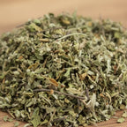 Feuilles de damiana séchées vert pâle en vrac sur surface en bois.