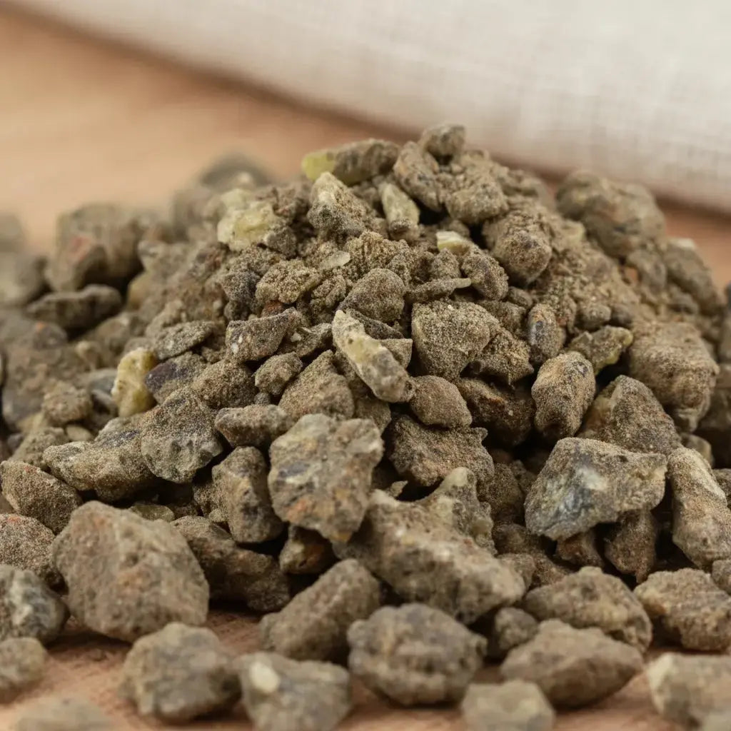 Gros plan sur un monticule de morceaux de résine d'Encens Djaoui Noir, montrant des grains irréguliers de couleur brun-gris foncé et terreux, avec une texture granuleuse.