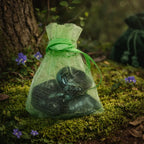 Pochette en organza vert clair contenant plusieurs petites pierres d'émeraude polies d'un vert sombre et mystérieux, posée sur un lit de mousse forestière.