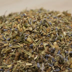 Gros plan sur un mélange d’encens aux herbes, grains de résine et petites fleurs violettes séchées.