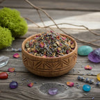 Bol en bois gravé rempli de mélange d’encens pour le chakra du cœur, avec herbes et pétales colorés entouré de cristaux sur une table en bois.