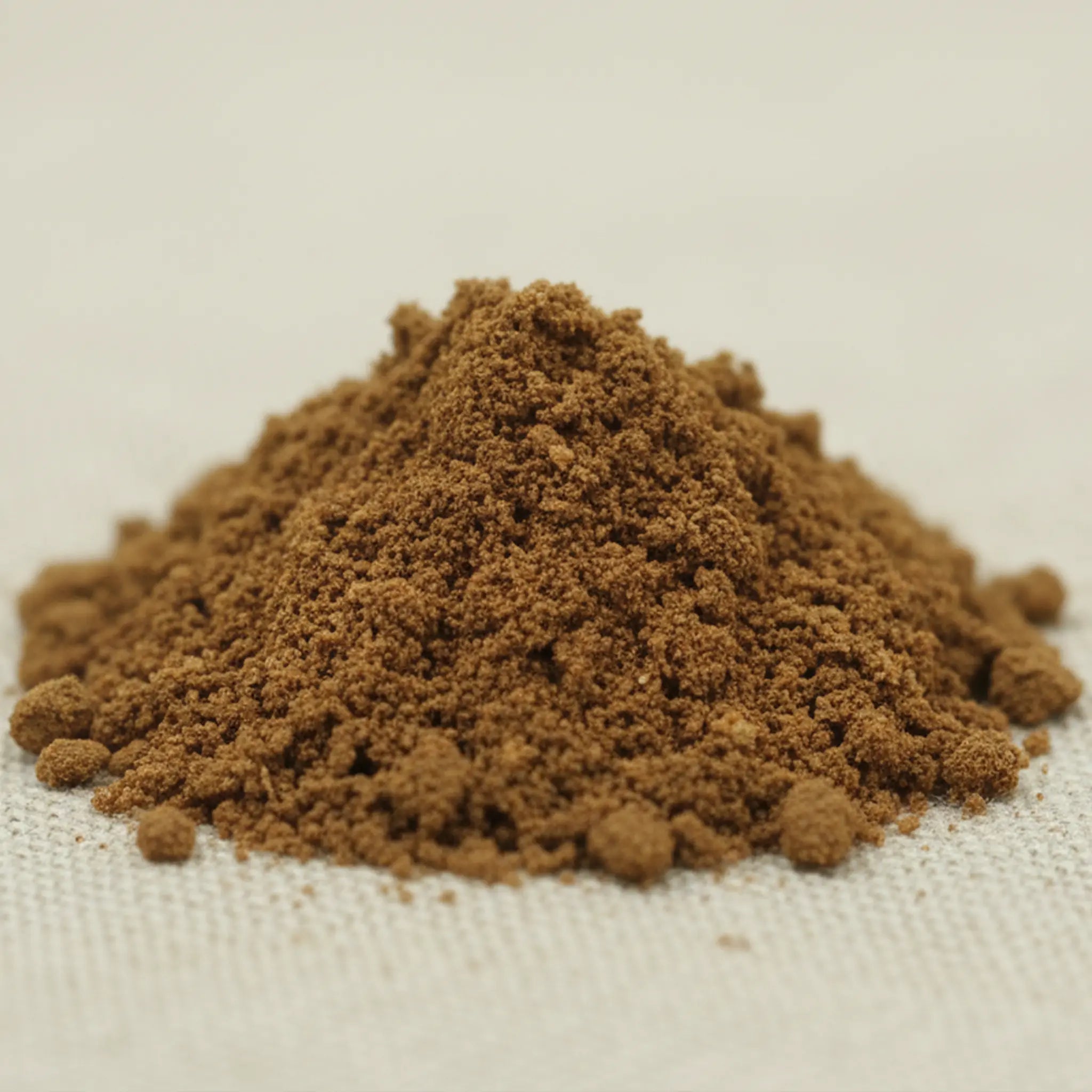 Tas de poudre d’encens nard de l’Himalaya brun à grain fin sur tissu clair.