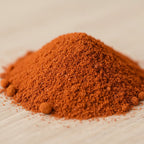 Tas de poudre de santal rouge orangé à grain fin sur surface en bois claire.