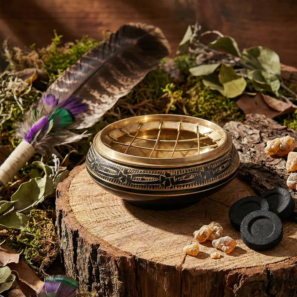 Brûle Encens Coupe laiton noir et doré posé sur une souche avec une plume et des résines.