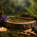Éteignoir rituel avec une cloche en laiton doré gravée d'une Fleur de Vie et un manche en bois sombre, posé sur une tranche de bois entourée de fleurs violettes et de bois de Palo Santo.