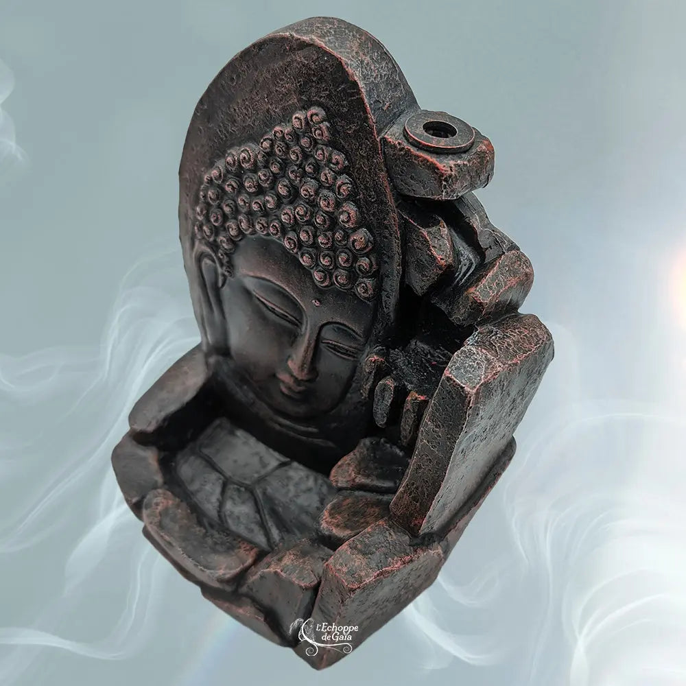 Porte-encens backflow noir patiné cuivre effet pierre, Bouddha et rochers, vue en biais sur fond bleu fumé, logo « L’Echoppe de Gaïa ».