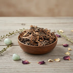 Coupelle en bois remplie de feuilles de frangipanier séchées brun foncé sur table en bois grise décorée de cristaux et pétales.