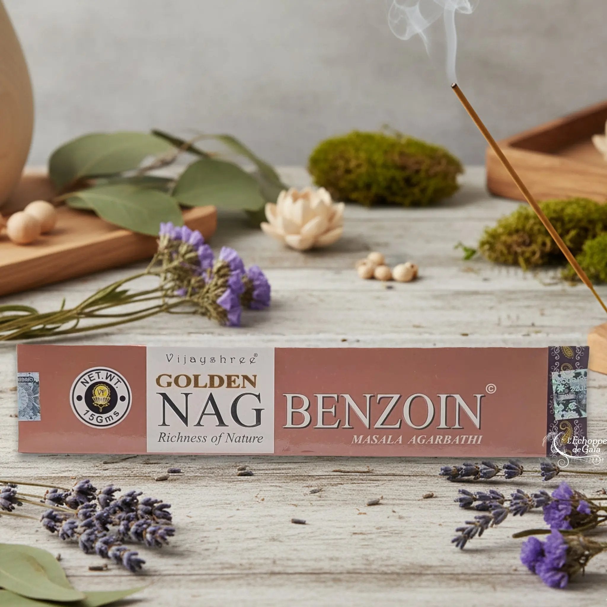 Boîte d'encens Vijayshree Golden Nag "Benzoin" Masala Agarbathi, posée sur une table avec de la lavande et un bâton d'encens fumant.