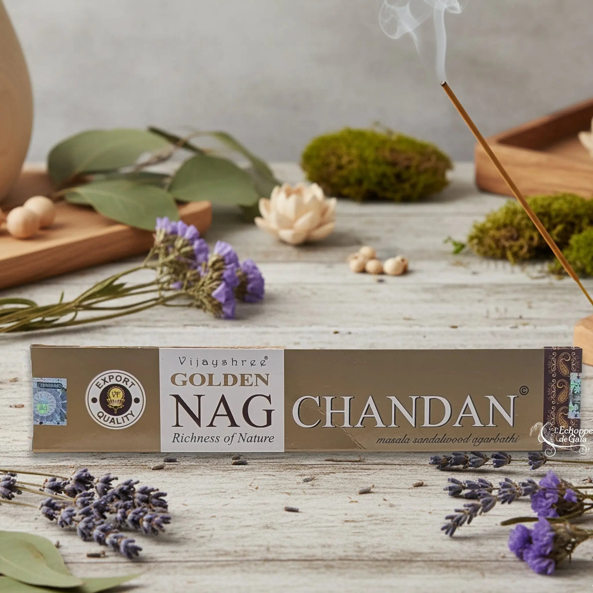 Boîte d'encens Vijayshree Golden Nag "Chandan" Masala Sandalwood Agarbathi, posée sur une table avec de la lavande et un bâton d'encens fumant.