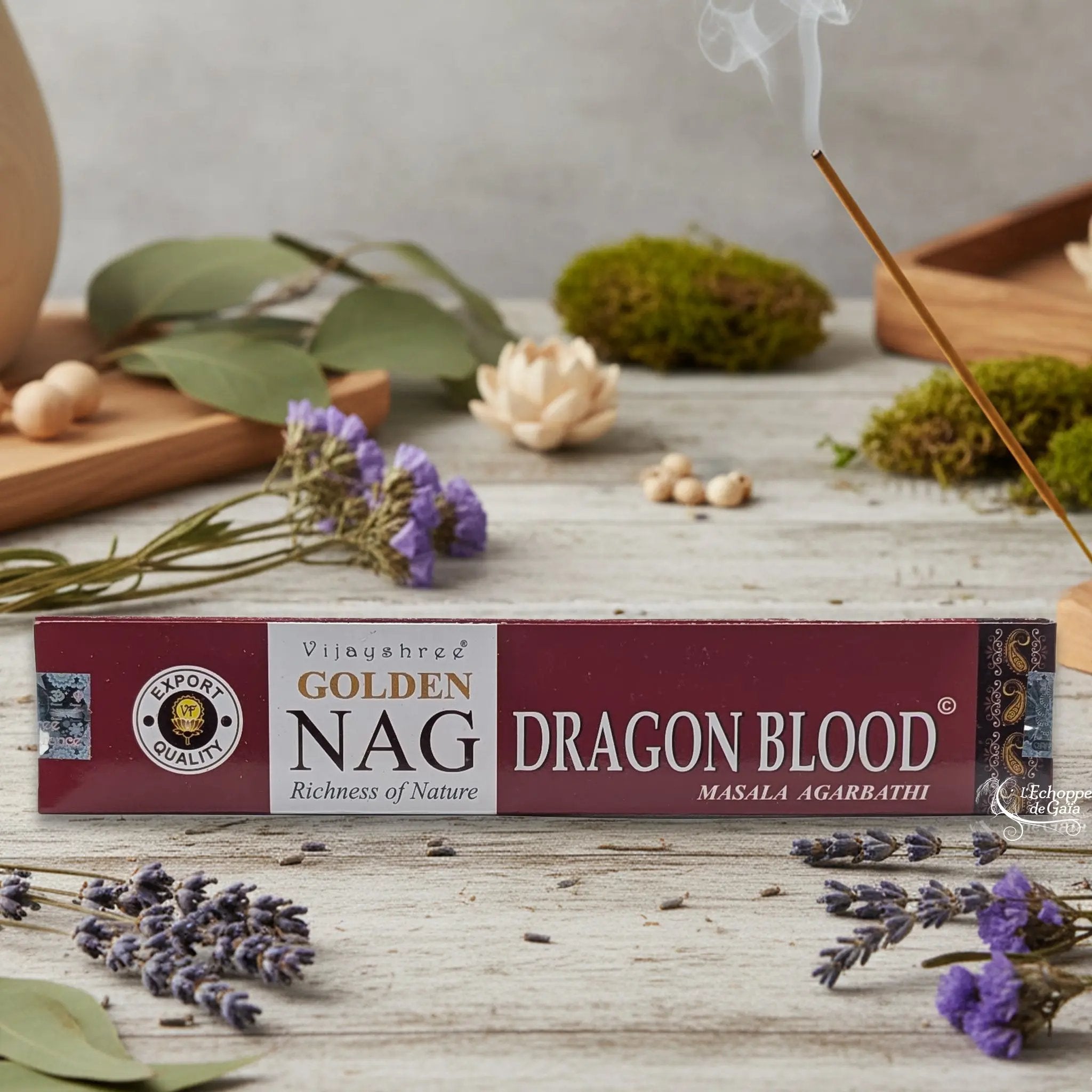 Boîte d'encens Vijayshree Golden Nag "Dragon Blood" Masala Agarbathi, posée sur une table avec de la lavande et un bâton d'encens fumant.