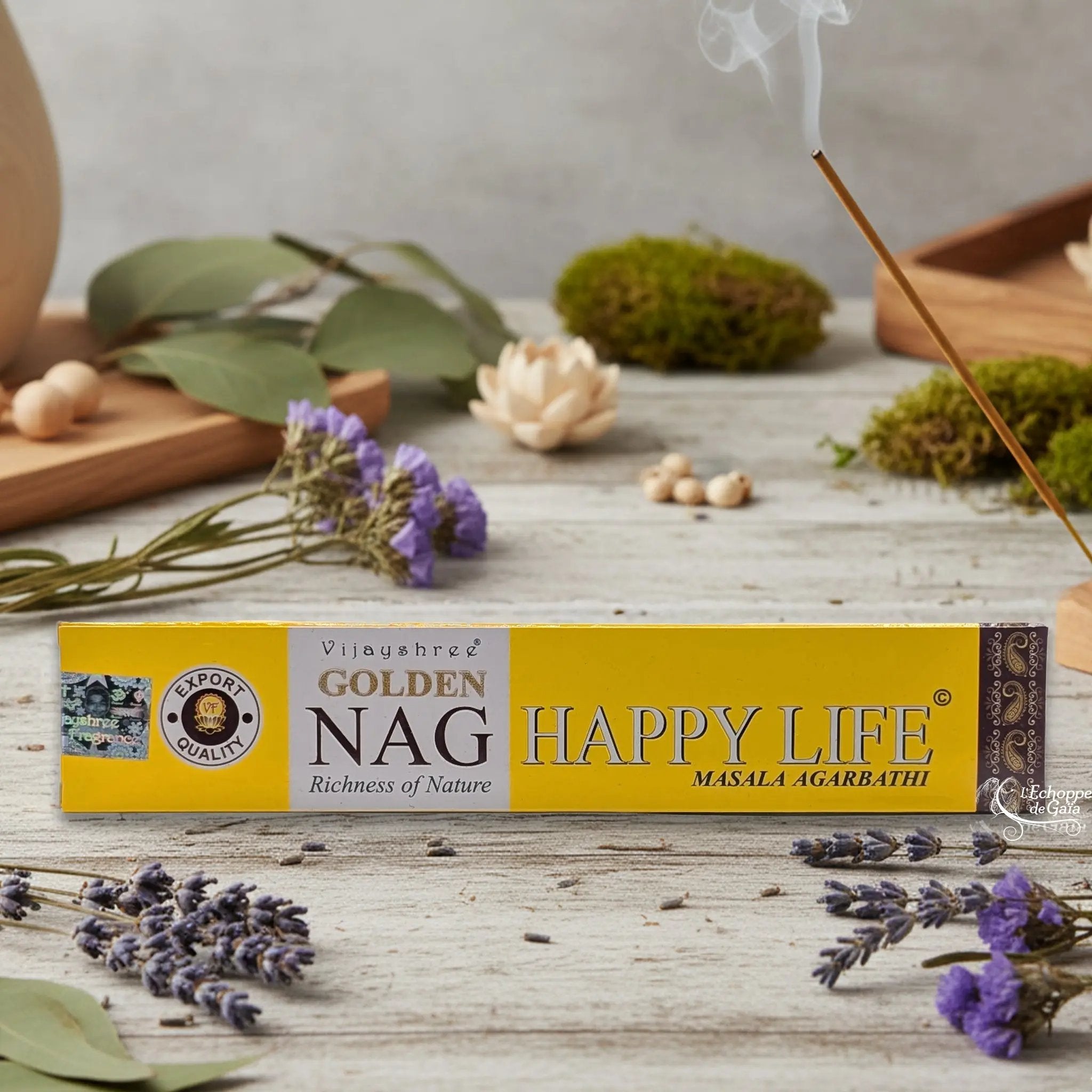 Boîte d'encens Vijayshree Golden Nag "Happy Life" Masala Agarbathi, posée sur une table avec de la lavande et un bâton d'encens fumant.