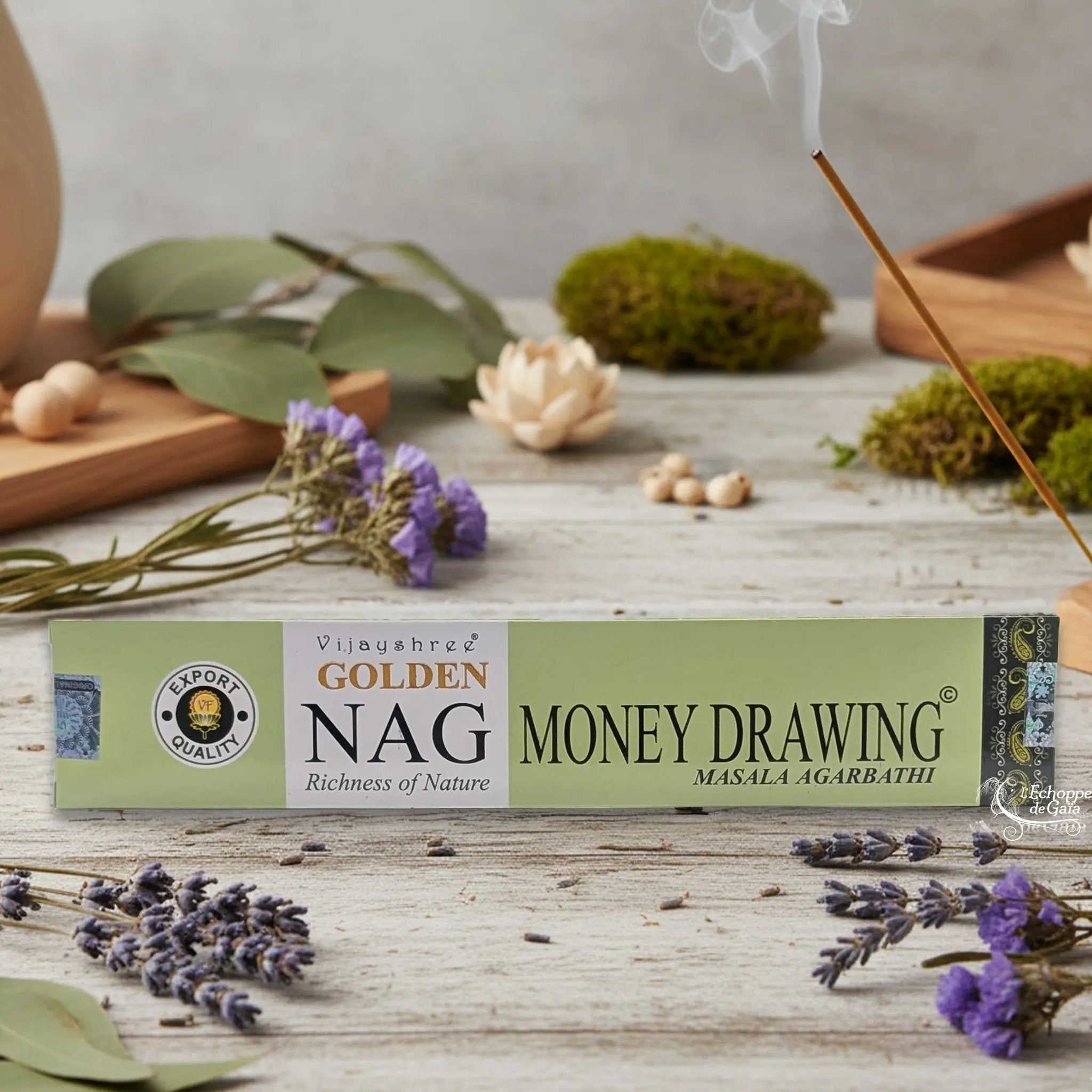 Boîte d'encens Vijayshree Golden Nag "Money Drawing" Masala Agarbathi, posée sur une table avec de la lavande et un bâton d'encens fumant.