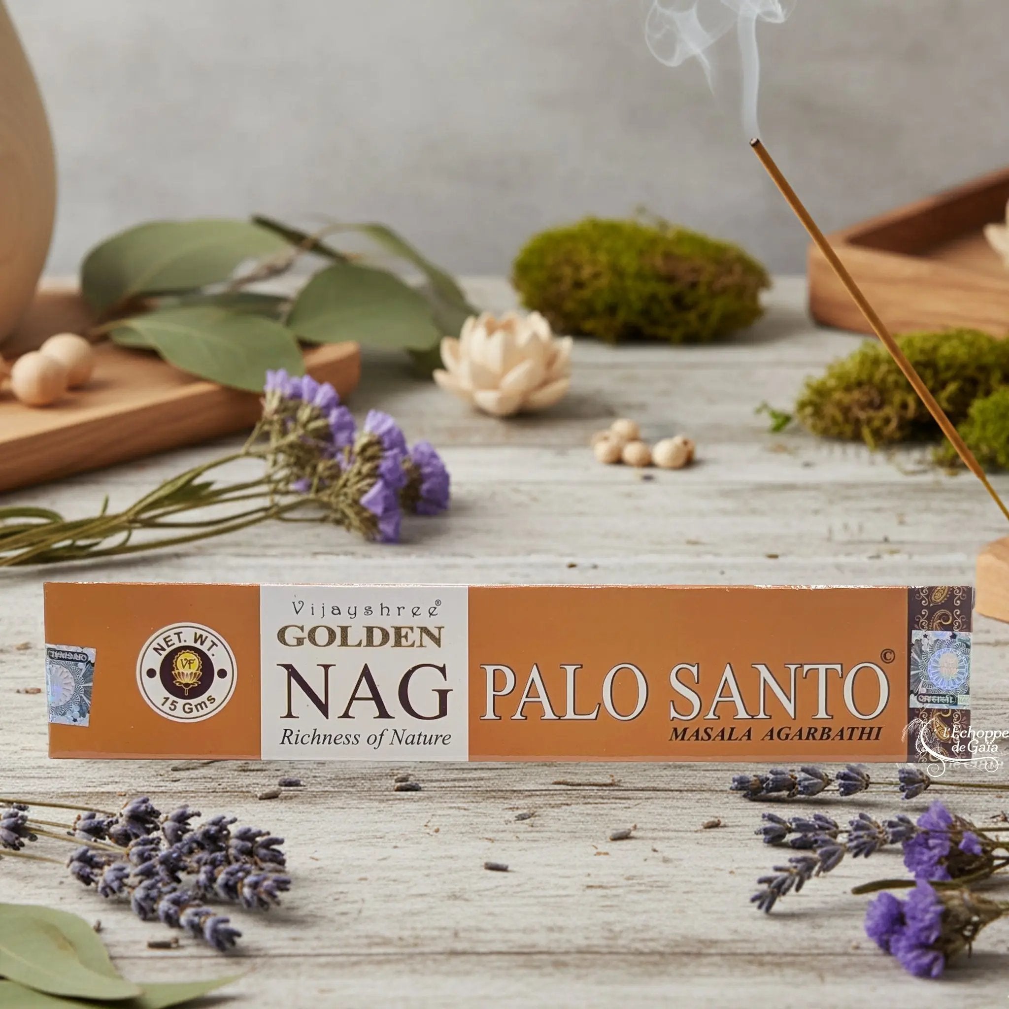 Boîte d'encens Vijayshree Golden Nag "Palo Santo" Masala Agarbathi, posée sur une table avec de la lavande et un bâton d'encens fumant.
