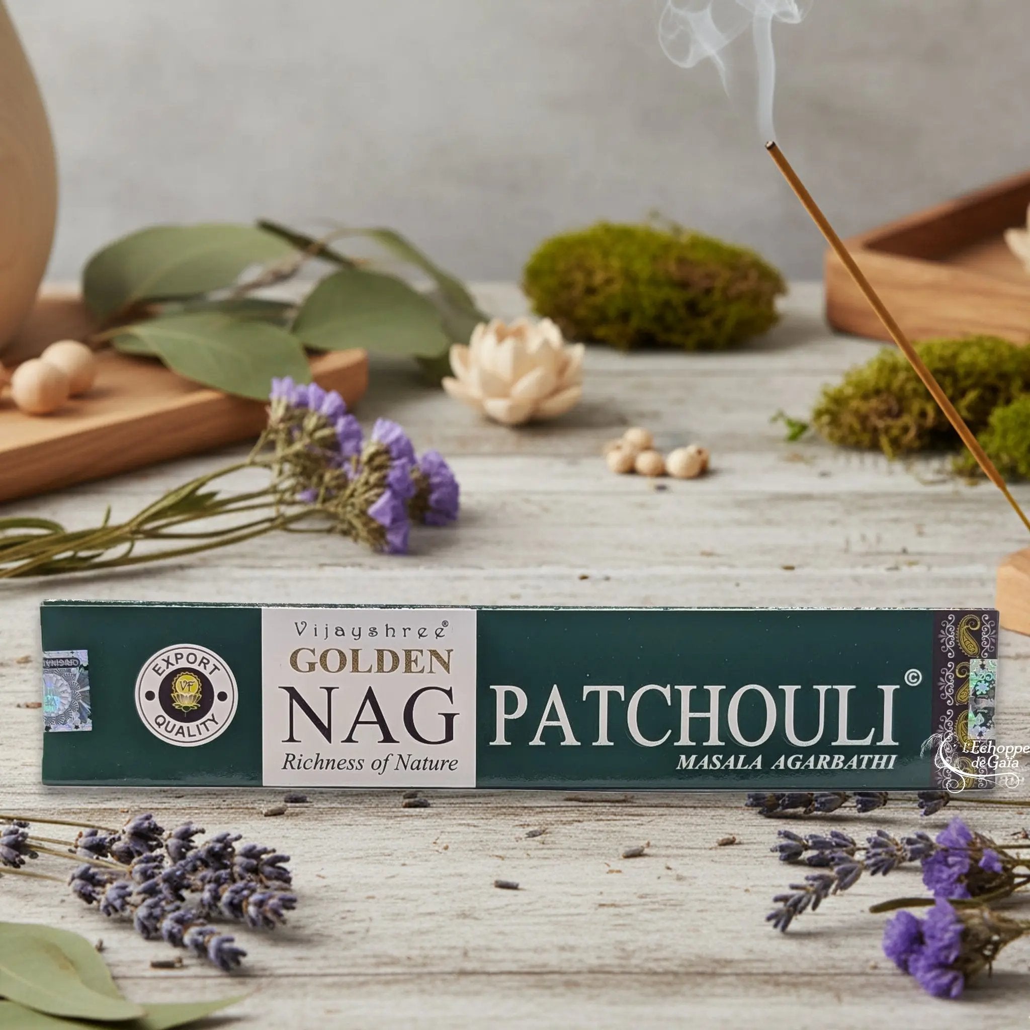 Boîte d'encens Vijayshree Golden Nag "Patchouli" Masala Agarbathi, posée sur une table avec de la lavande et un bâton d'encens fumant.