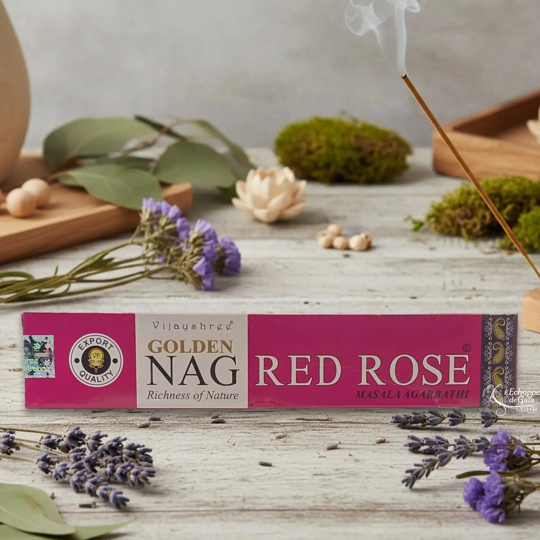 Boîte d'encens Vijayshree Golden Nag "Red Rose" Masala Agarbathi, posée sur une table avec de la lavande et un bâton d'encens fumant.