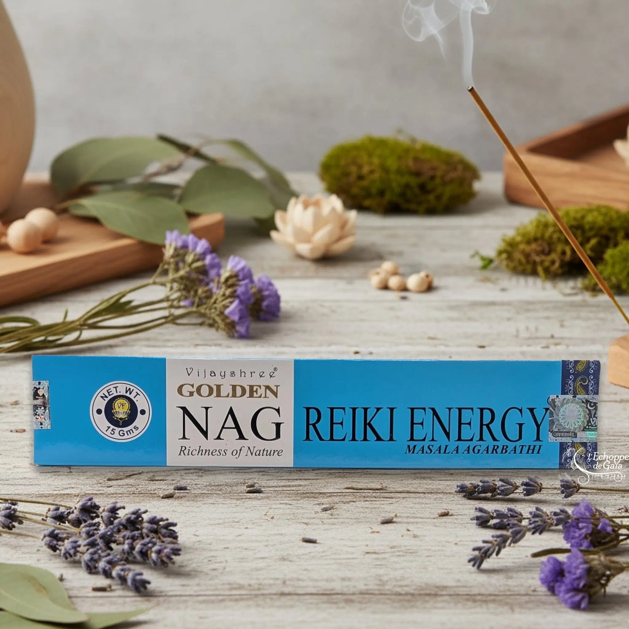 Boîte d'encens Vijayshree Golden Nag "Reiki Energy" Masala Agarbathi, posée sur une table avec de la lavande et un bâton d'encens fumant.