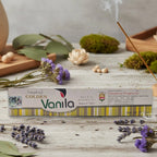 Boîte d'encens Vijayshree Golden "Vanila" Masala Agarbathi, posée sur une table avec de la lavande et un bâton d'encens fumant.