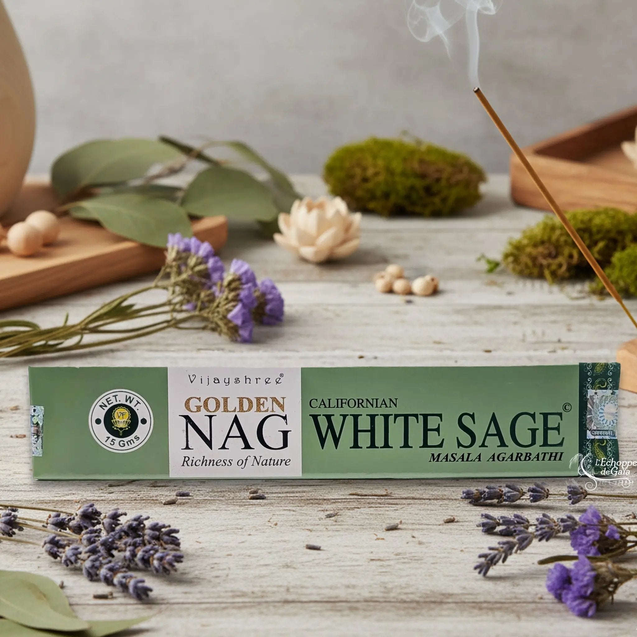 Boîte d'encens Vijayshree Golden Nag "Californian White Sage" Masala Agarbathi, posée sur une table avec de la lavande et un bâton d'encens fumant.