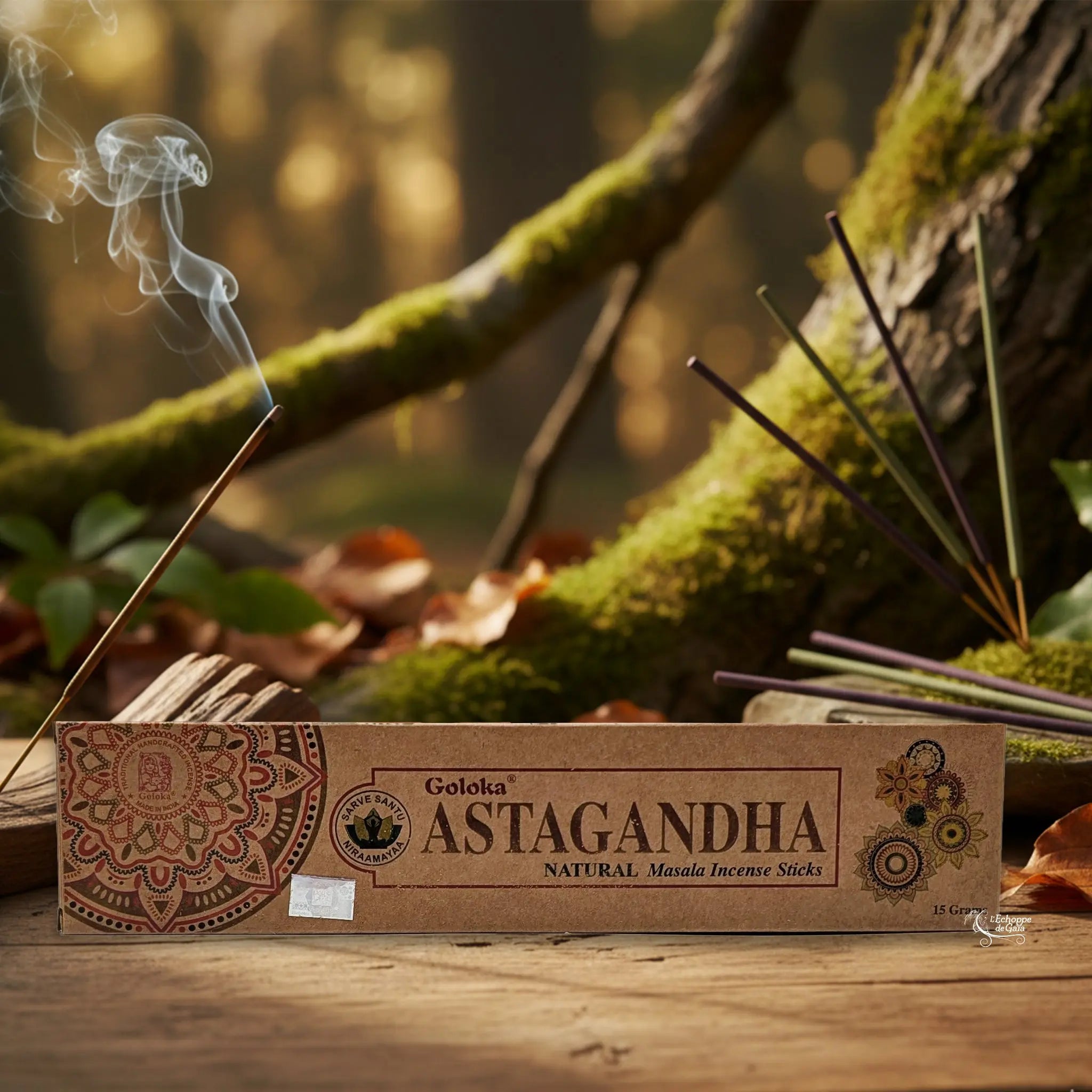 Boîte d’encens Goloka « Astagandha » posée sur une table en bois, avec un bâtonnet allumé dégageant de la fumée, sur fond de forêt moussue.