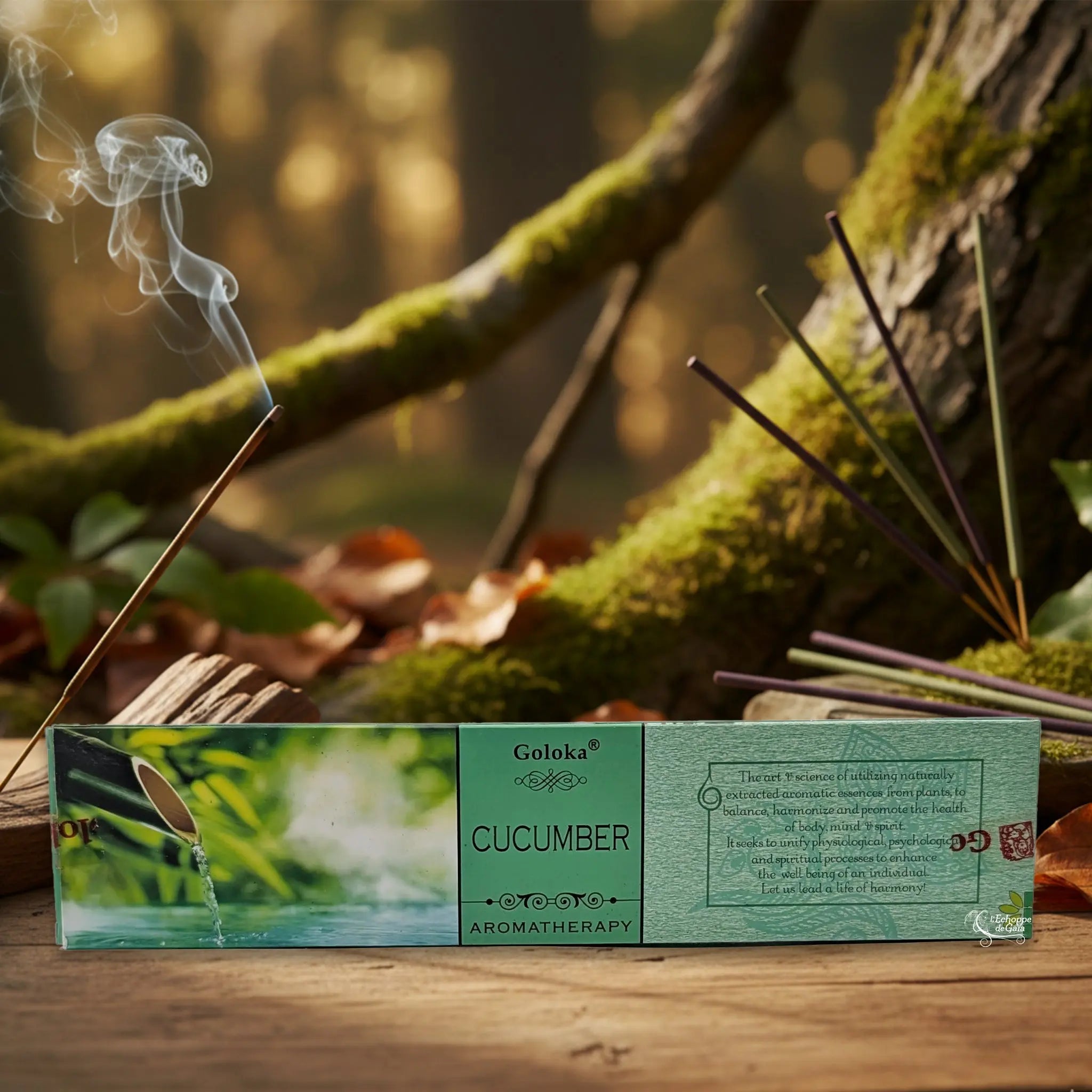 Boîte d’encens Goloka « Cucumber » (aromatherapy) posée sur une table en bois, avec un bâtonnet allumé et de la fumée, sur fond de forêt moussue.