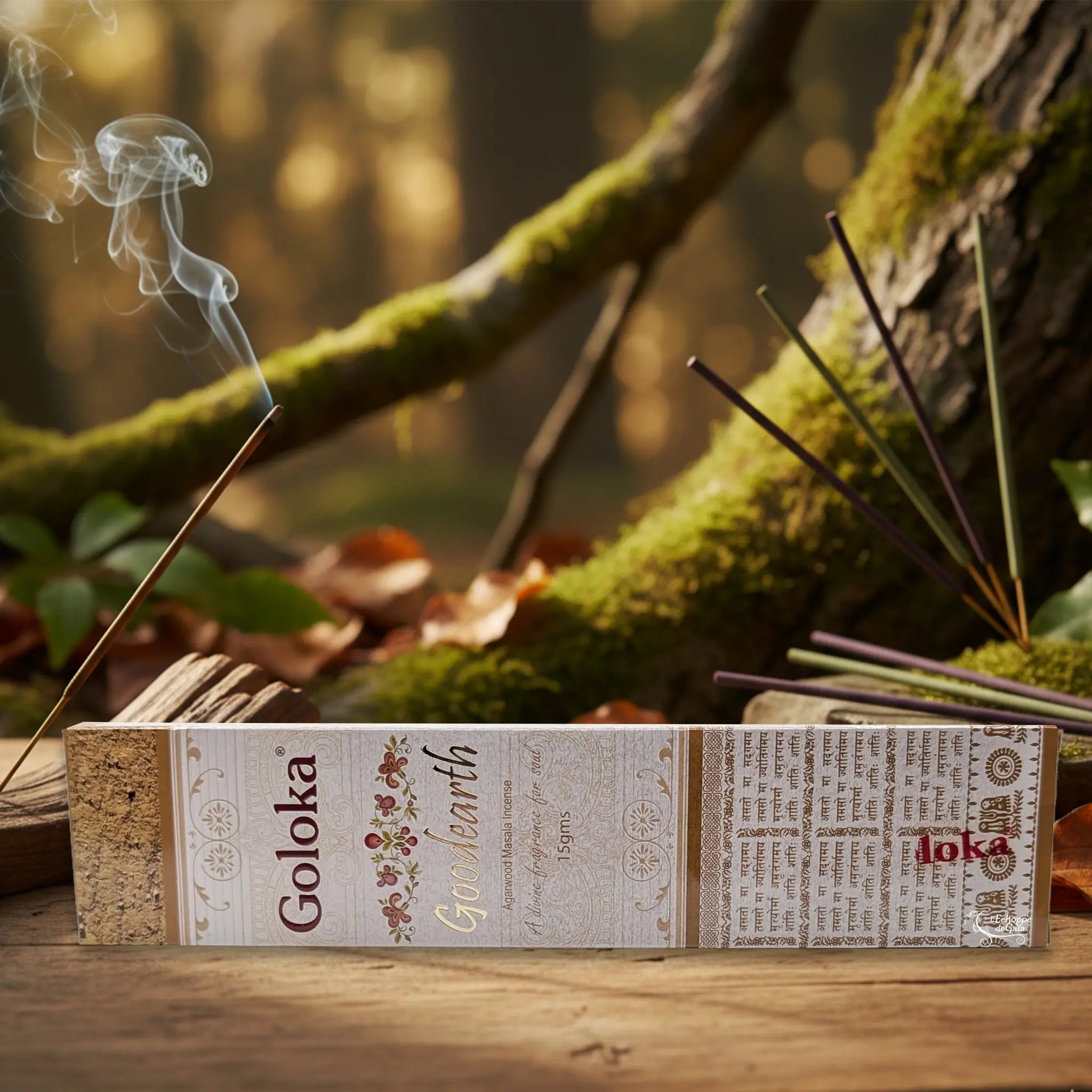 Boîte d’encens Goloka « Good Earth » posée sur une table en bois, avec un bâtonnet allumé dégageant une fine fumée, en décor de forêt moussue.