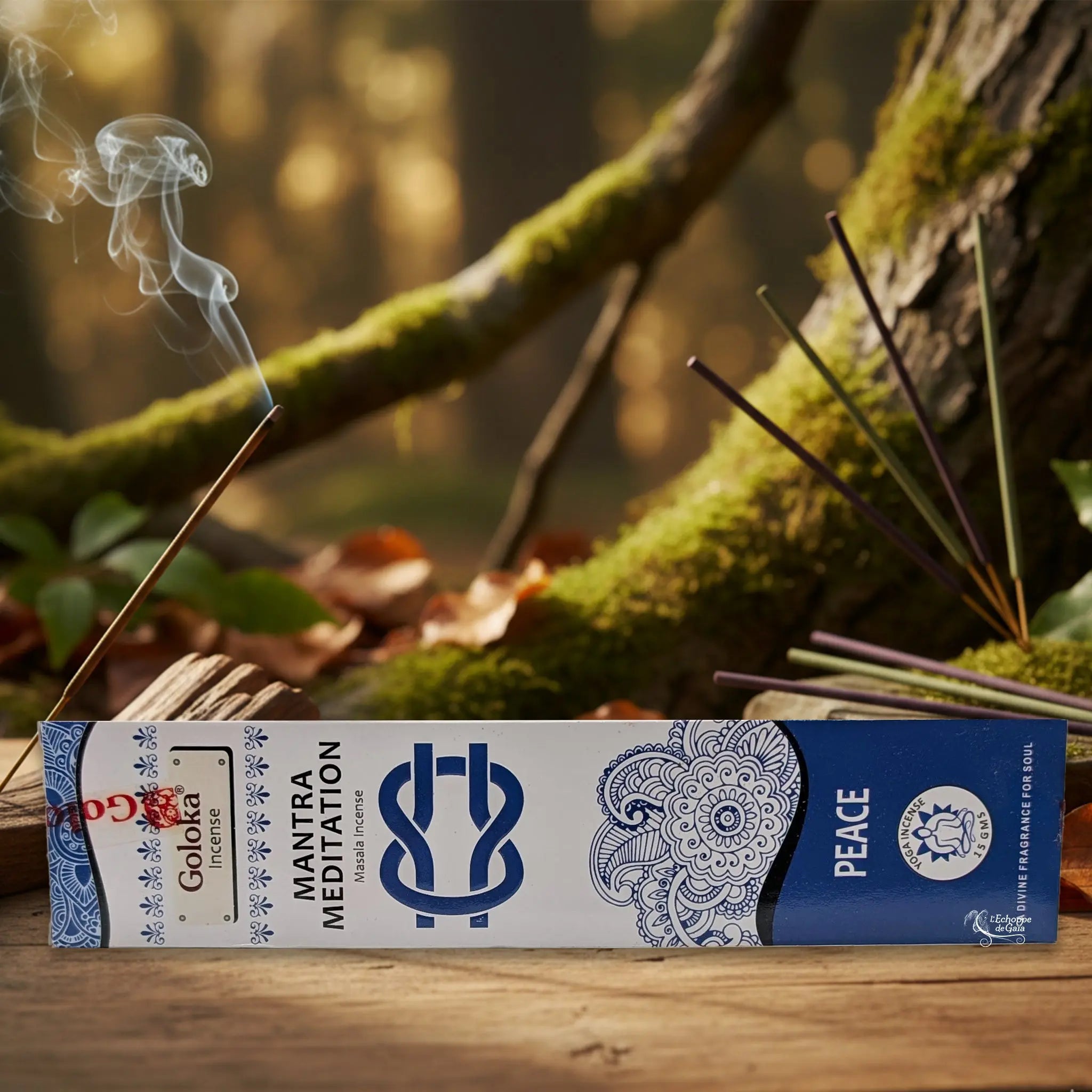 Boîte d’encens Goloka « Mantra Meditation – Peace » posée sur une table en bois, avec un bâtonnet allumé et de la fumée, sur fond de forêt moussue.