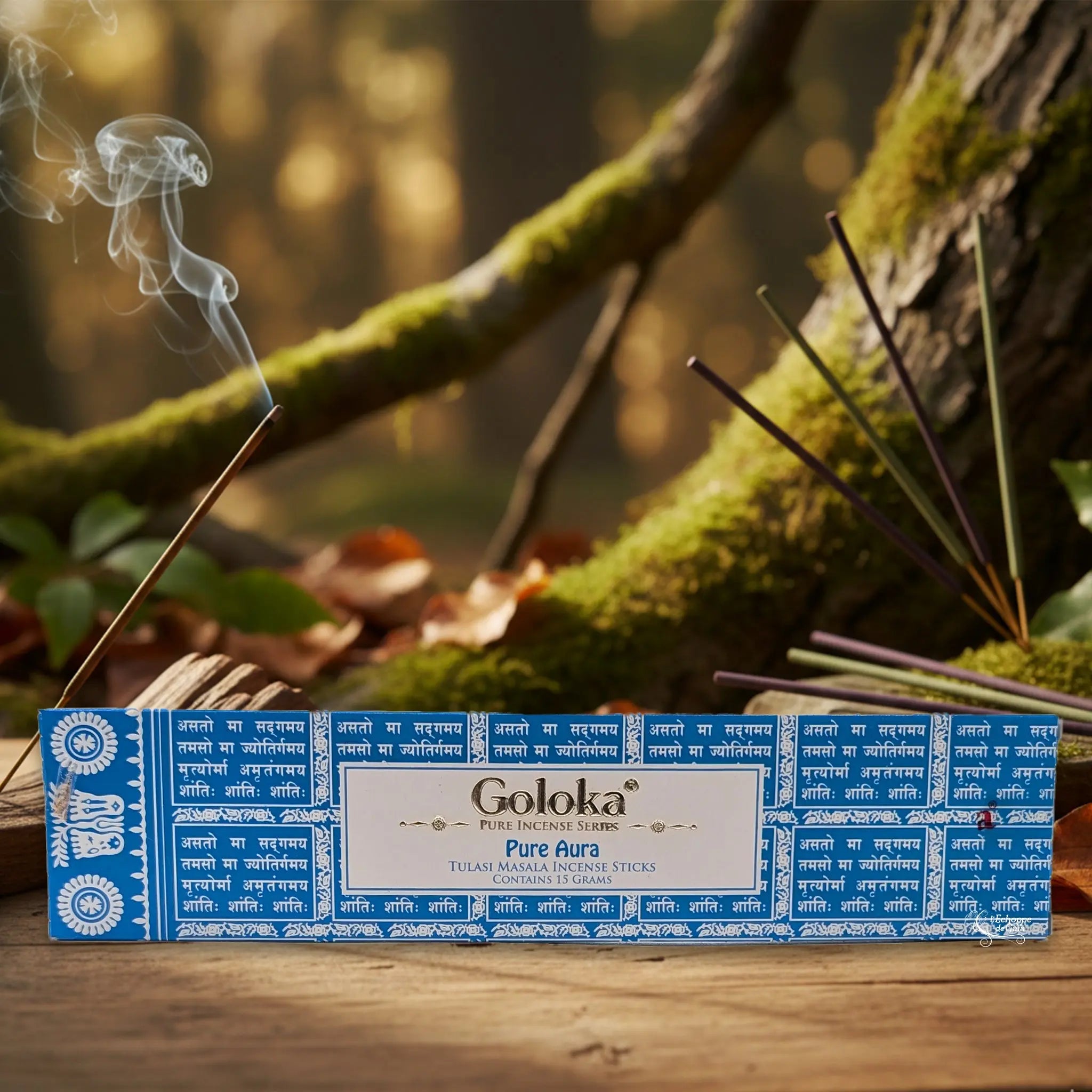 Boîte d’encens Goloka « Pure Aura » posée sur une table en bois, avec un bâtonnet allumé et sa fumée, sur fond de forêt moussue.