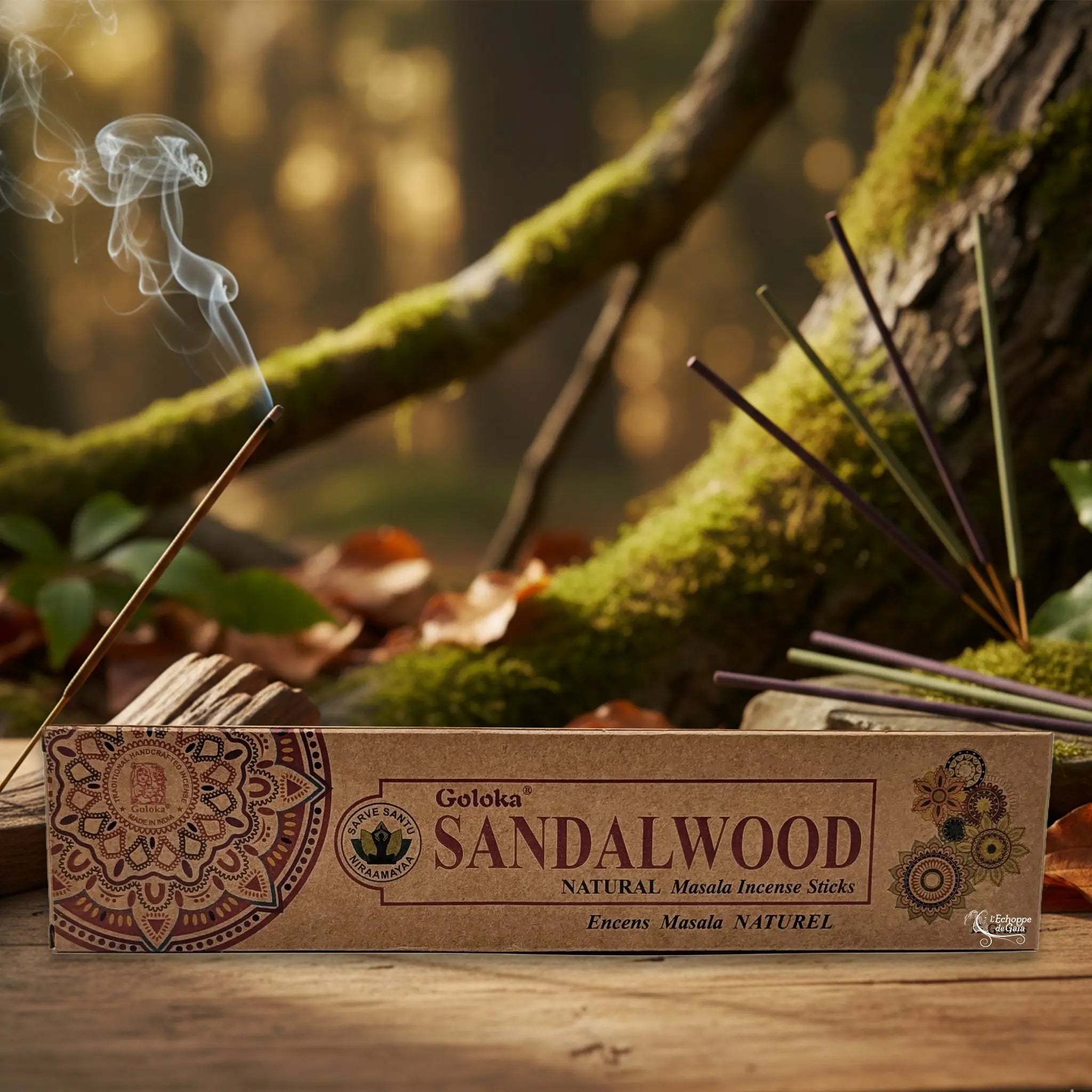 Boîte d’encens Goloka « Sandalwood » posée sur une table en bois, avec un bâtonnet allumé et de la fumée, sur fond de forêt moussue.