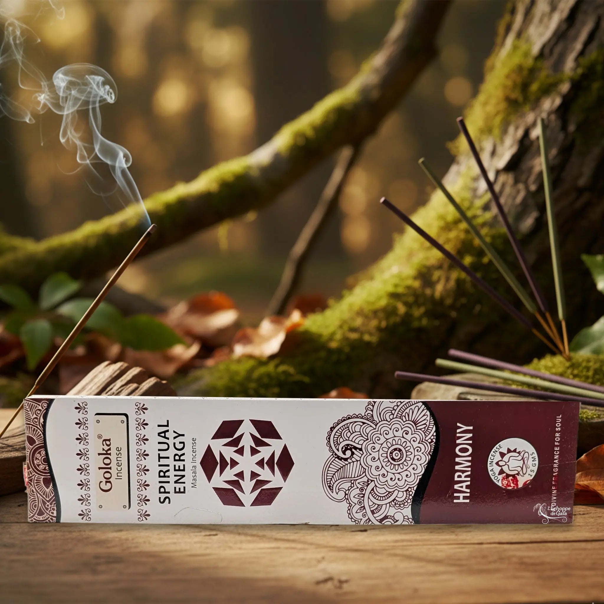 Boîte d’encens Goloka « Spiritual Energy – Harmony » posée sur une table en bois, avec un bâtonnet allumé et sa fumée, sur fond de forêt moussue.