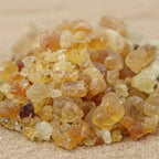 Gros plan sur des grains de résine d’encens en gomme arabique ambrés et translucides sur fond sableux.