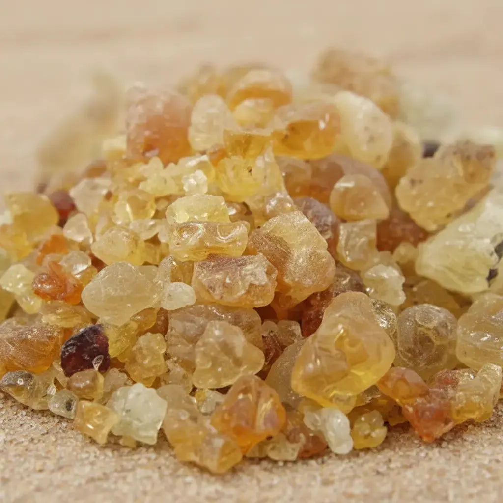 Gros plan sur des grains de résine d’encens en gomme arabique ambrés et translucides sur fond sableux.