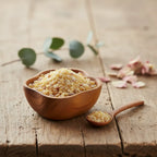 Grains de gomme de résine d'Élémi, de couleur jaune-ambre, dans un bol en bois clair avec une cuillère, sur une planche de bois rustique.