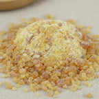 Gros plan sur un monticule de grains de résine d'Élémi, montrant de l'ambre clair mélangé à de la poudre de résine jaune pâle, sur un fond en tissu clair.
