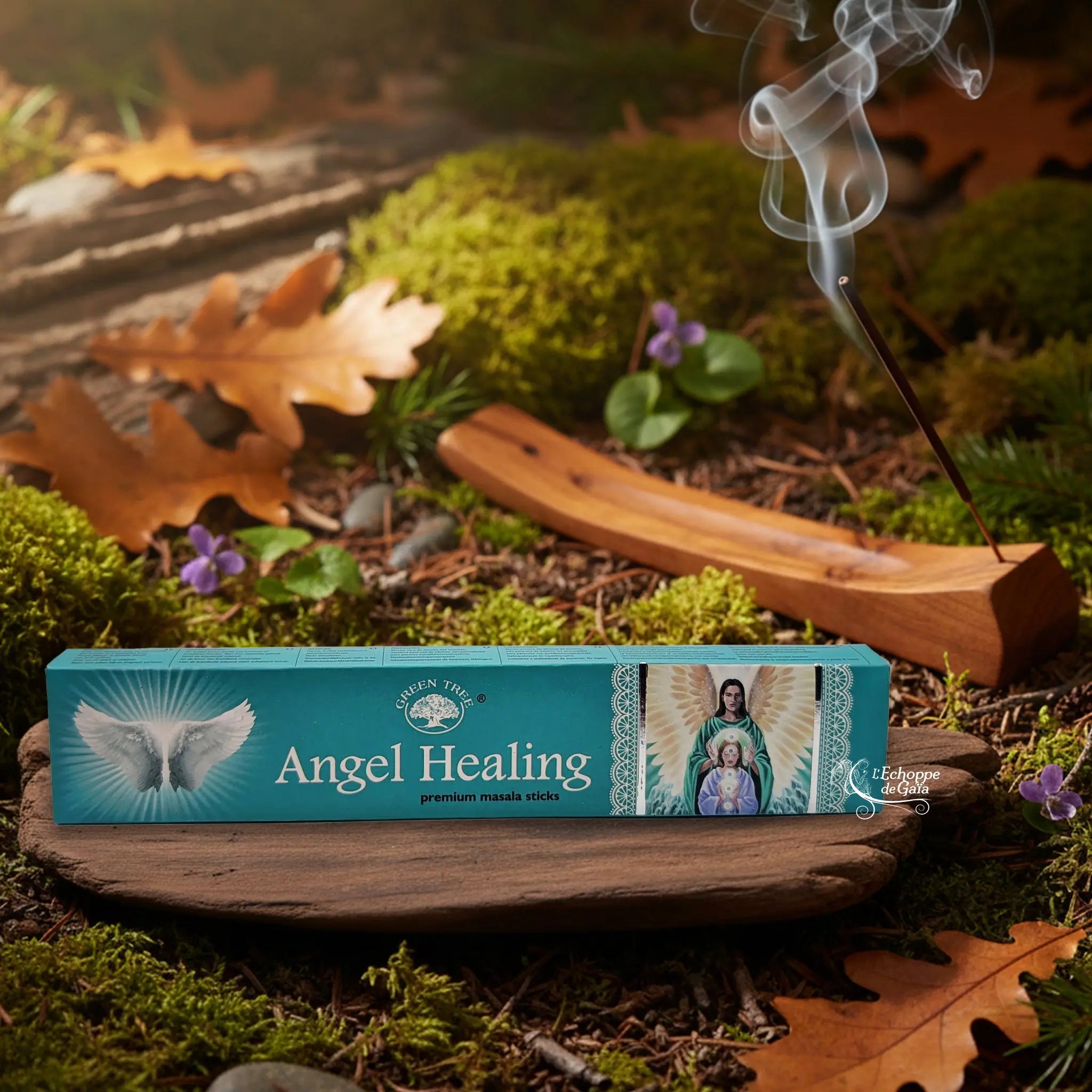 Boîte d’encens Green Tree “Angel Healing” posée sur un support en bois dans un décor de sous-bois automnal, avec au second plan un porte-encens en bois d’où s’élève une volute de fumée.