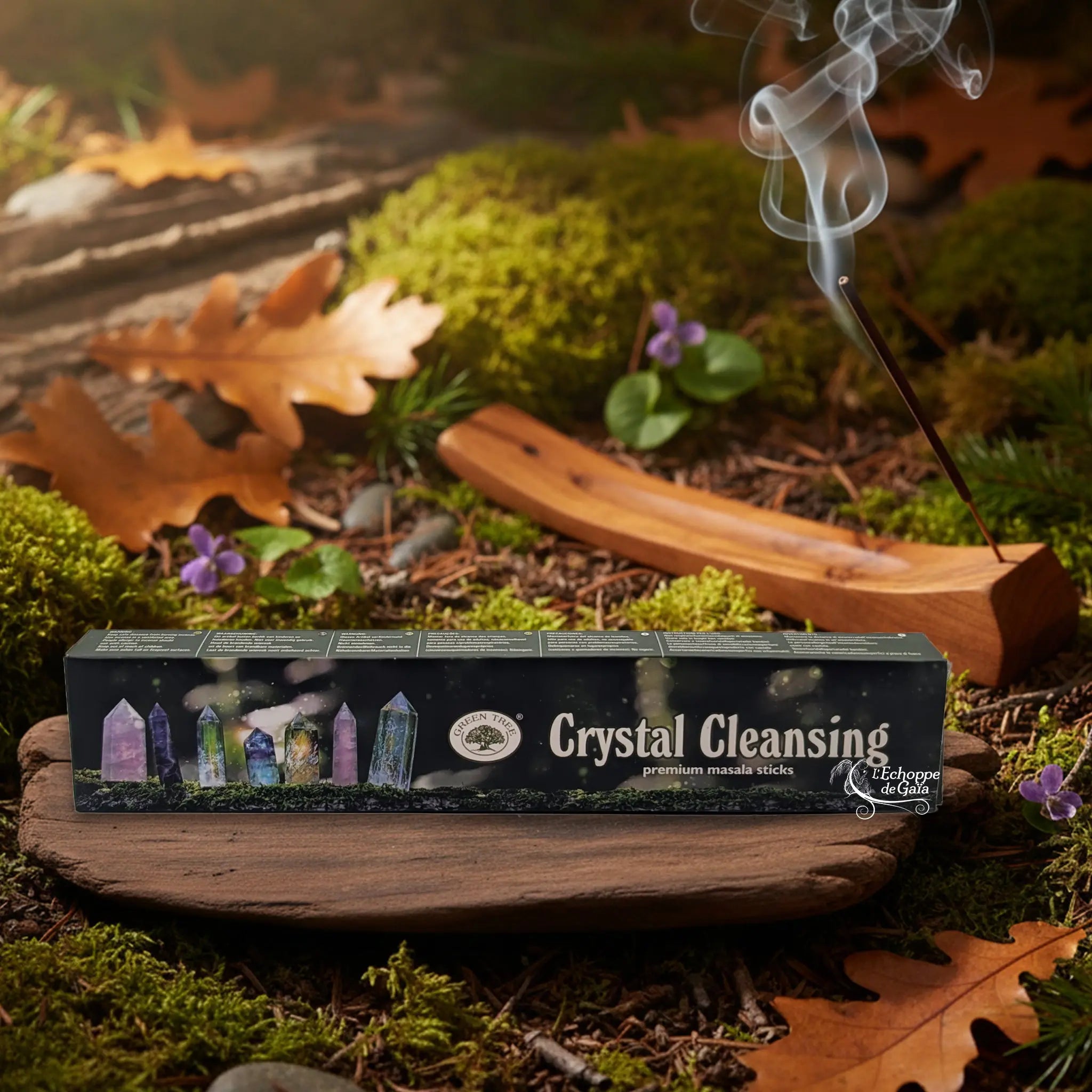 Boîte d’encens « Crystal Cleansing » Green Tree posée sur un lit de mousse en forêt, avec porte-encens en bois fumant à l’arrière-plan.