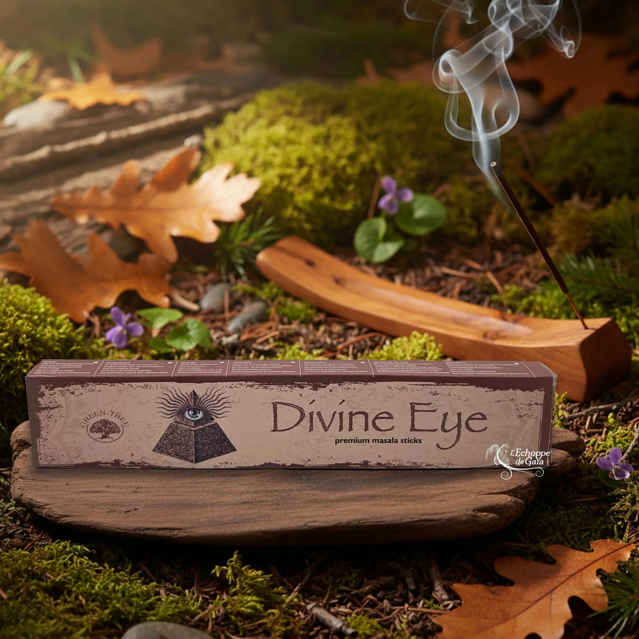 Boîte d’encens « Divine Eye » Green Tree posée sur un lit de mousse en forêt, avec porte-encens en bois fumant à l’arrière-plan.