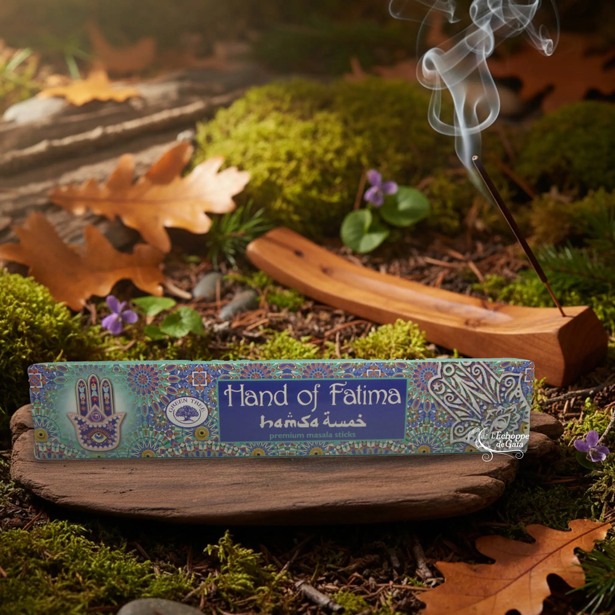 Boîte d’encens « Hand of Fatima » Green Tree posée sur un lit de mousse en forêt, avec porte-encens en bois fumant à l’arrière-plan.