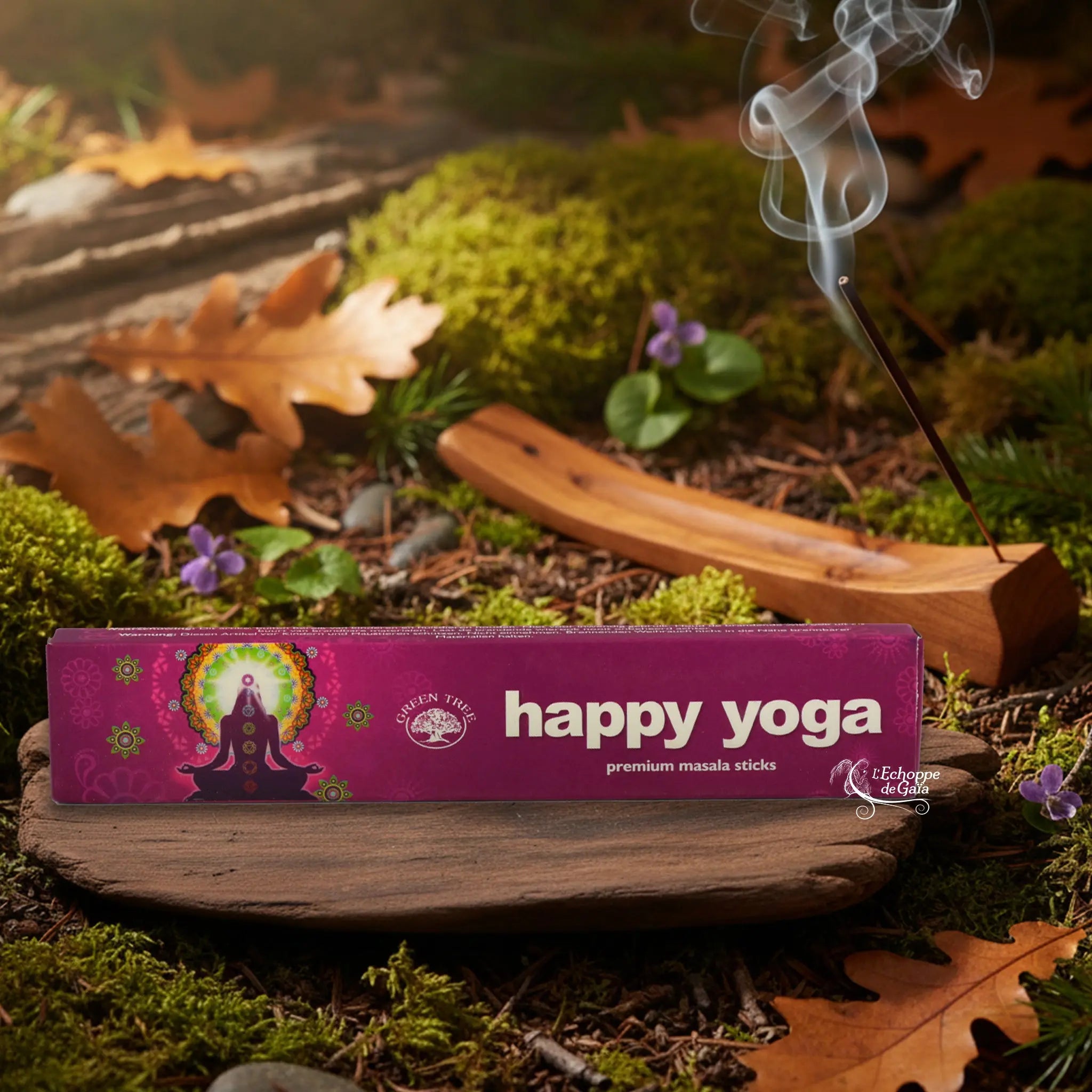 Boîte d’encens « Happy Yoga » Green Tree posée sur un lit de mousse en forêt, avec porte-encens en bois fumant à l’arrière-plan.