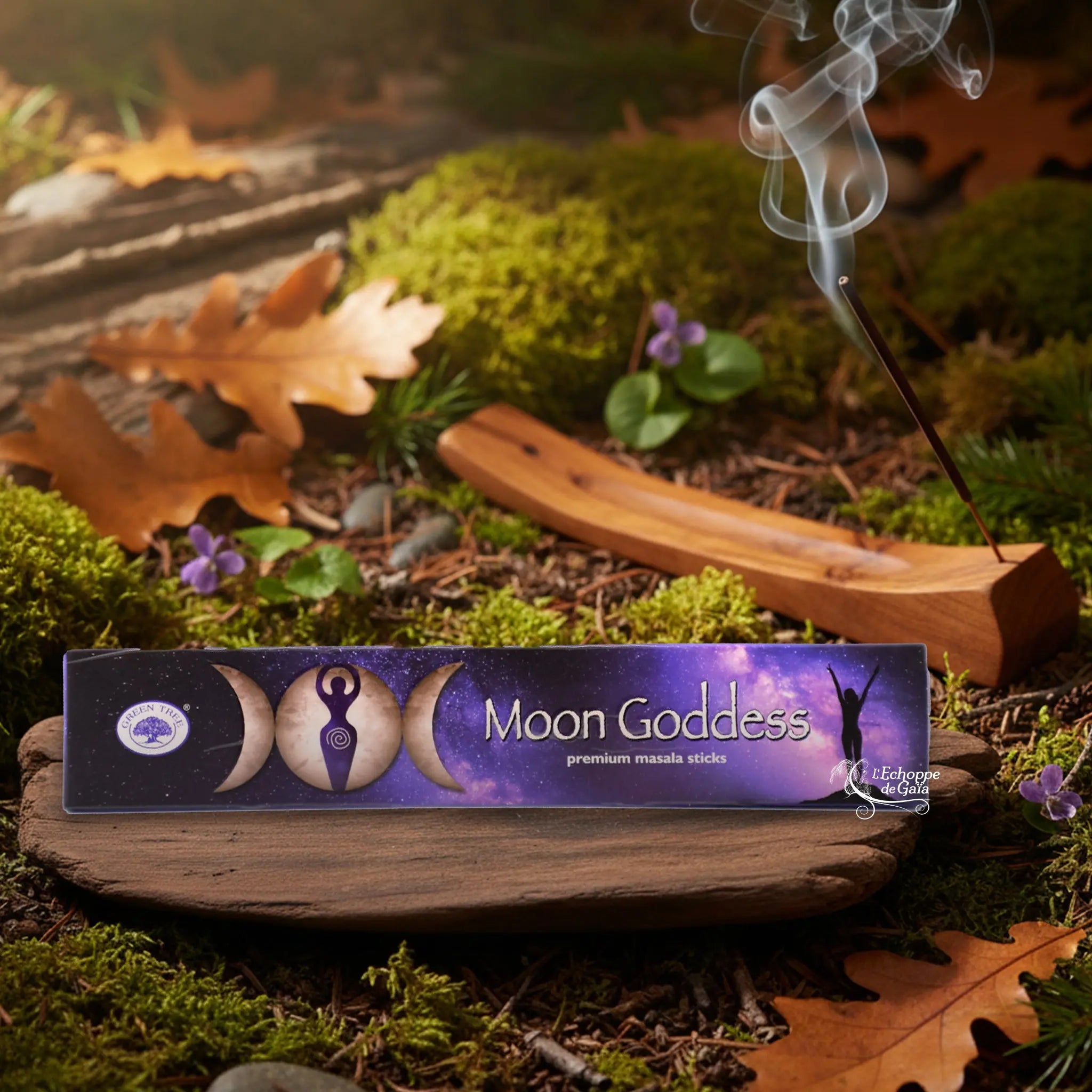 Boîte d’encens Green Tree “Moon Goddess” posée sur un support en bois, avec bâton d’encens fumant sur sol forestier.