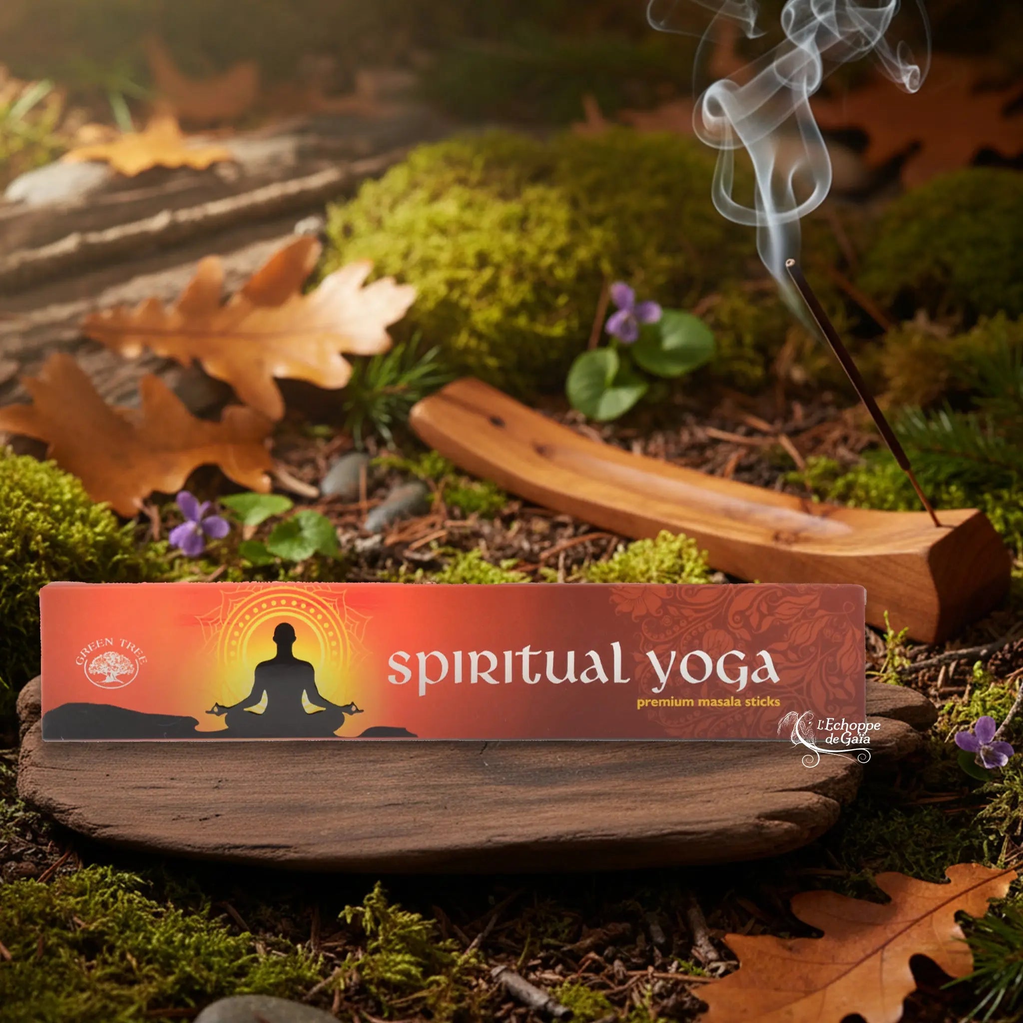 Boîte d’encens Green Tree “Spiritual Yoga” posée sur un support en bois, avec bâton d’encens fumant en arrière-plan sur sol forestier.