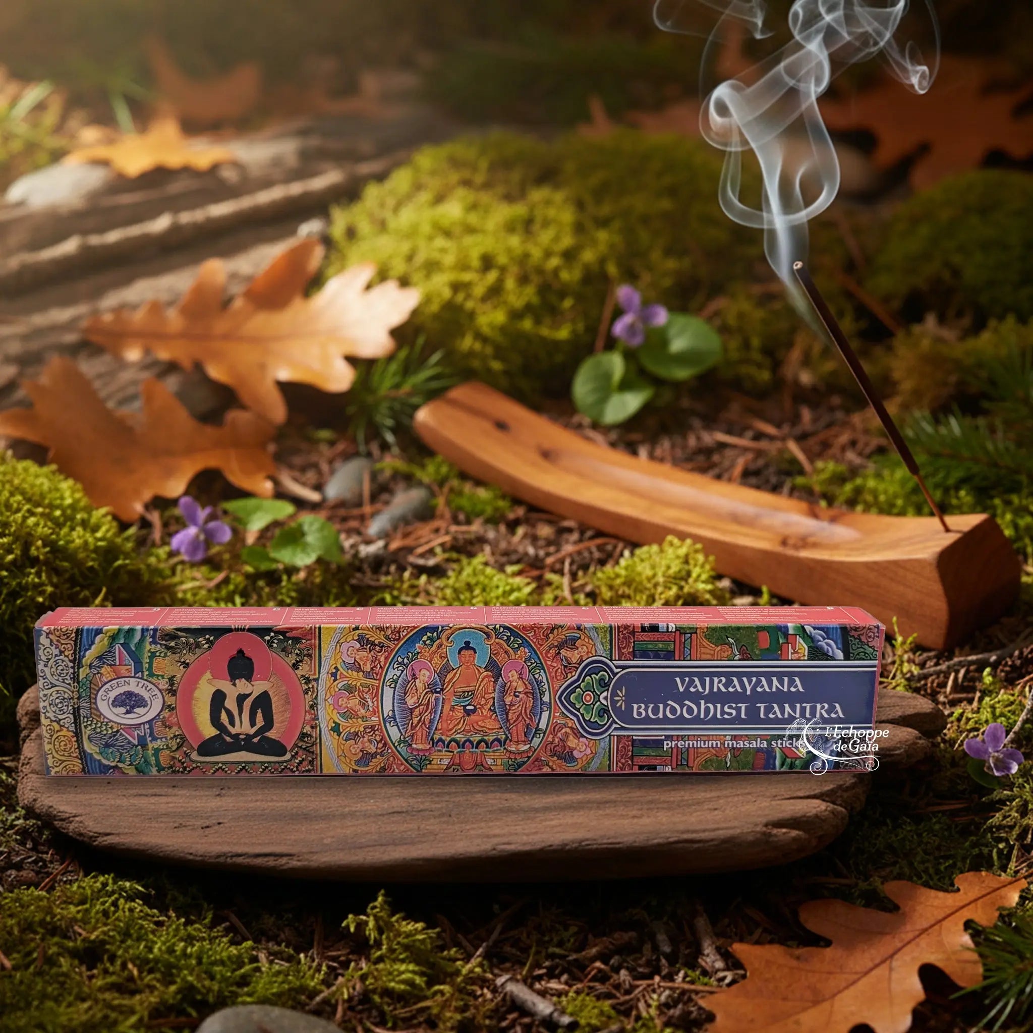 Boîte d’encens Green Tree “Vajrayana Buddhist Tantra” aux motifs bouddhistes colorés, posée sur une planche de bois au milieu de la mousse et des feuilles d’automne, avec un bâton d’encens fumant dans un porte-encens en bois à l’arrière-plan.