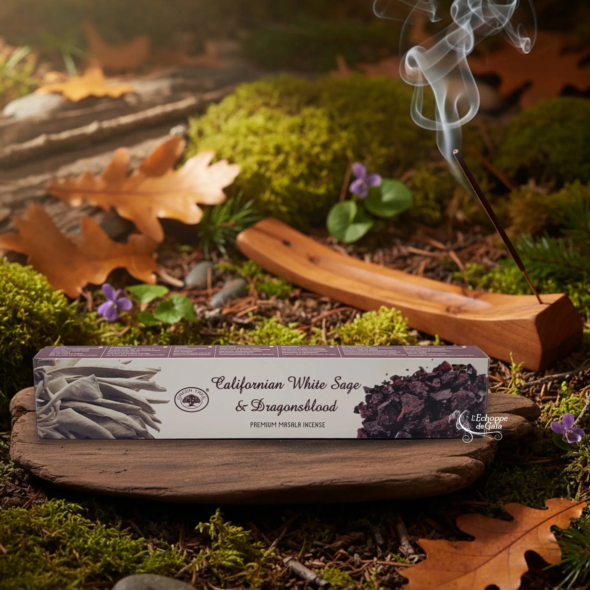 Boîte d’encens « Californian White Sage & Dragonsblood » Green Tree posée sur un lit de mousse en forêt, avec porte-encens en bois fumant à l’arrière-plan.