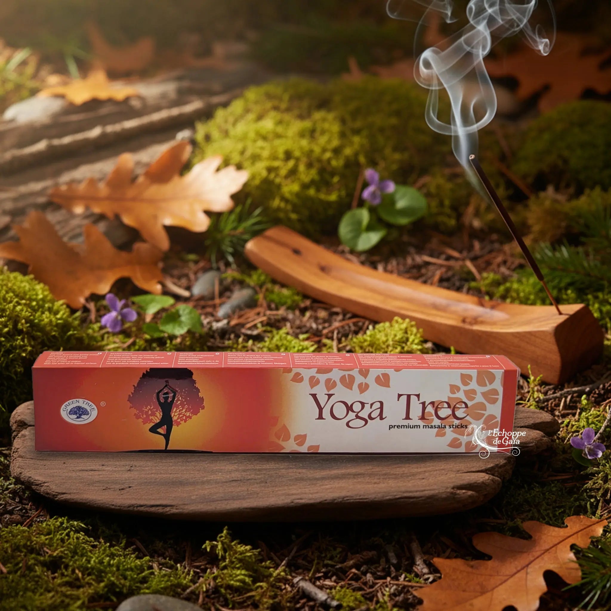Boîte d’encens Green Tree “Yoga Tree” posée sur un support en bois, dans un décor de sous-bois automnal avec un bâton d’encens fumant à l’arrière-plan.