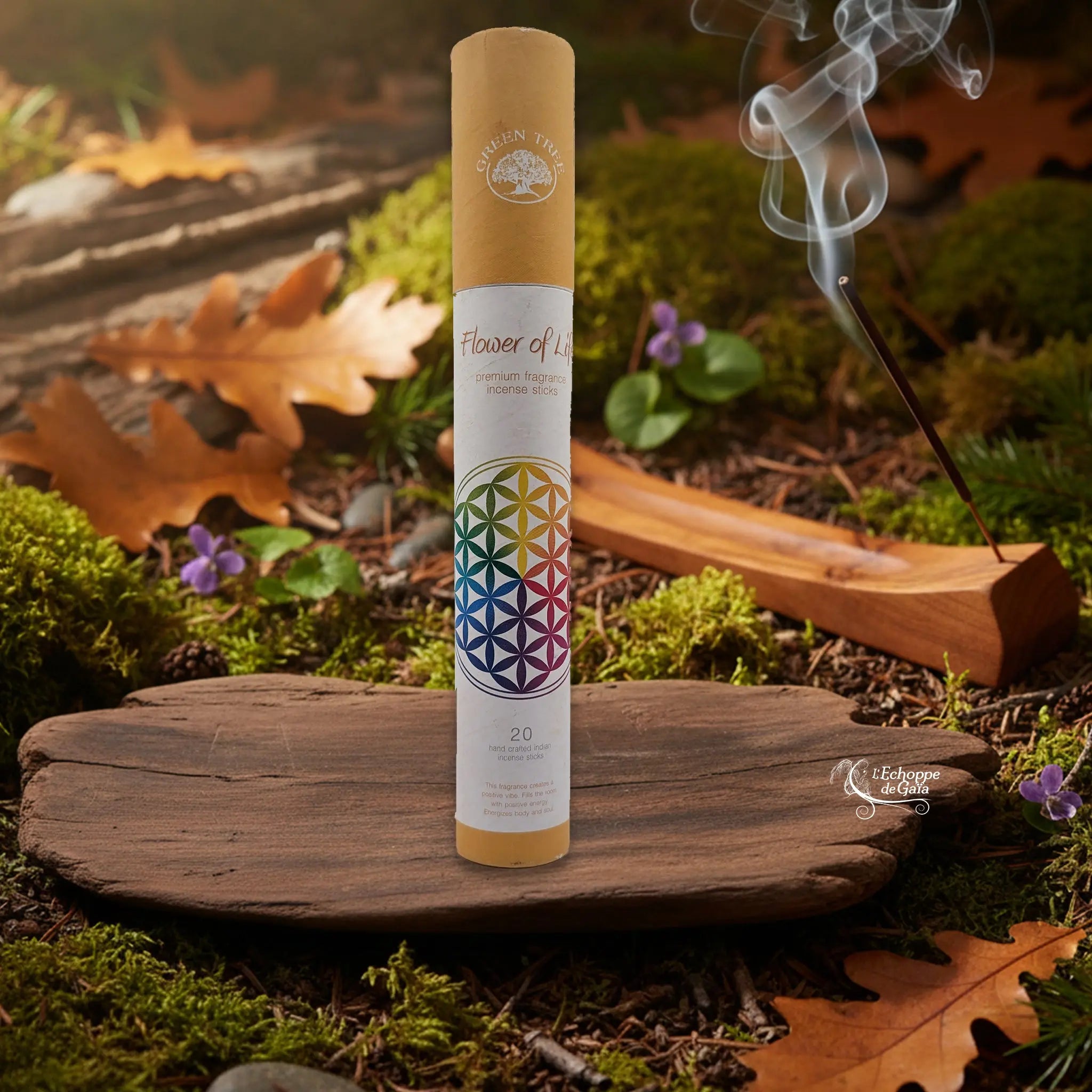 Tube d’encens Green Tree « Flower of Life » sur une tranche de bois, avec un bâtonnet allumé dans un porte-encens en bois et de la fumée, décor nature.