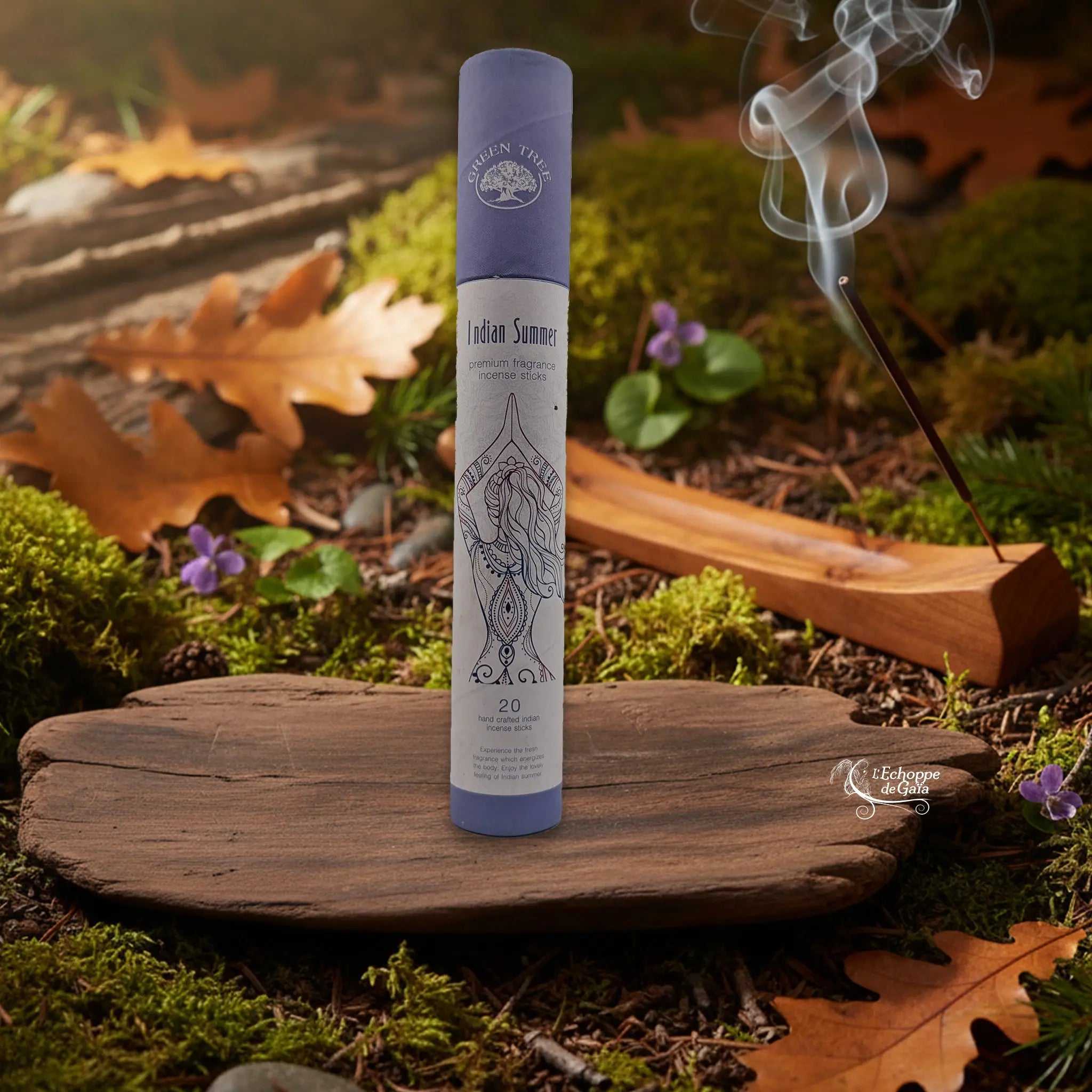 Tube d’encens Green Tree « Indian Summer » sur une tranche de bois, avec un bâtonnet allumé dans un porte-encens en bois et de la fumée, décor nature.