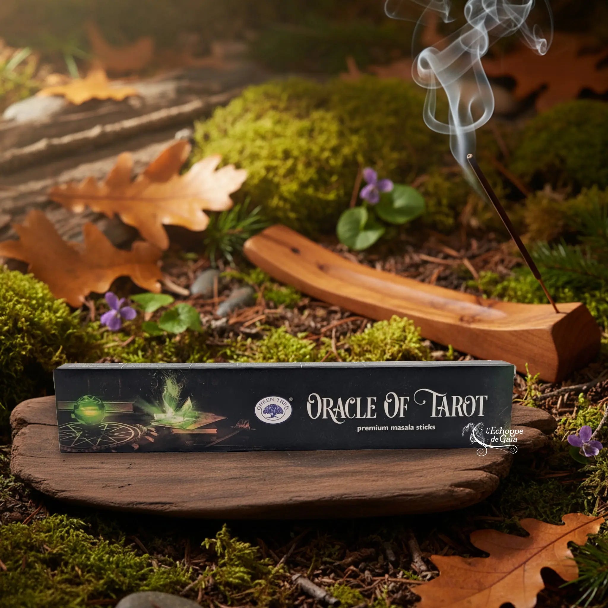 Boîte d’encens Green Tree « Oracle of Tarot » posée sur une tranche de bois, avec un bâtonnet allumé dans un porte-encens en bois et de la fumée, décor nature.